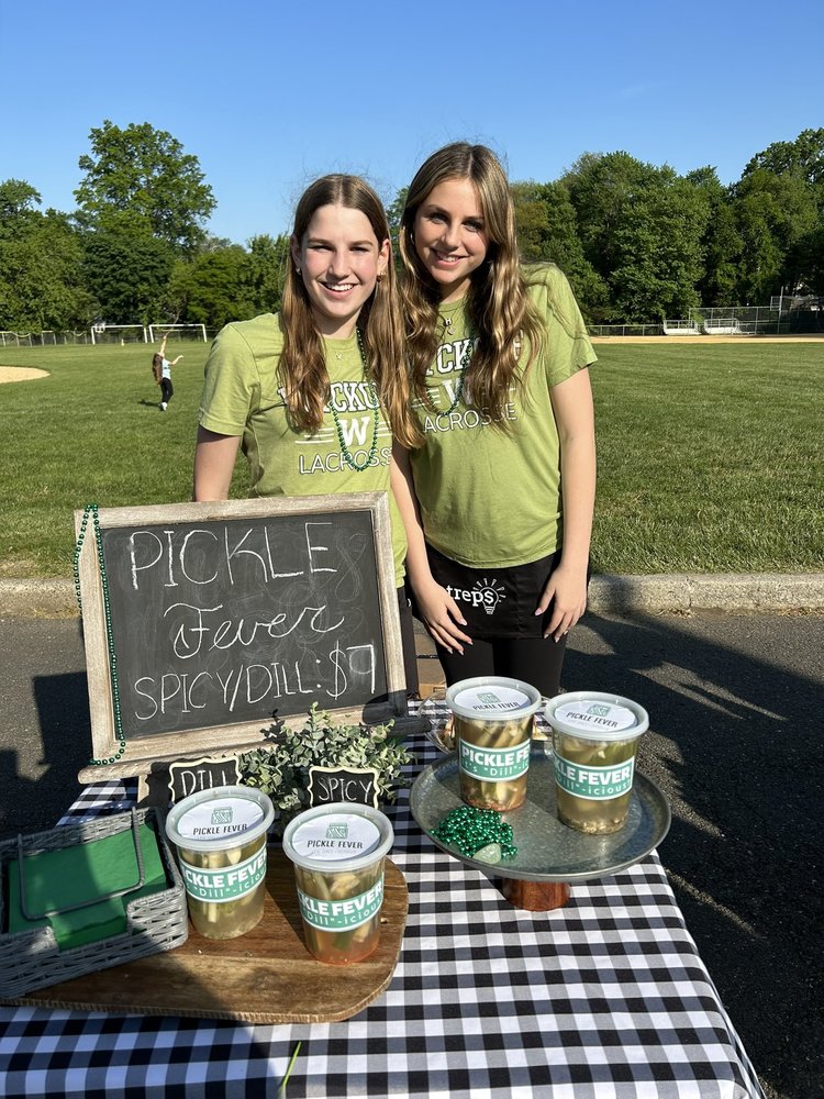 two middle school students selling pickles at outdoor marketplace