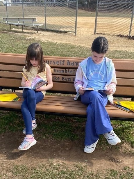 Two girls reading on bench outside