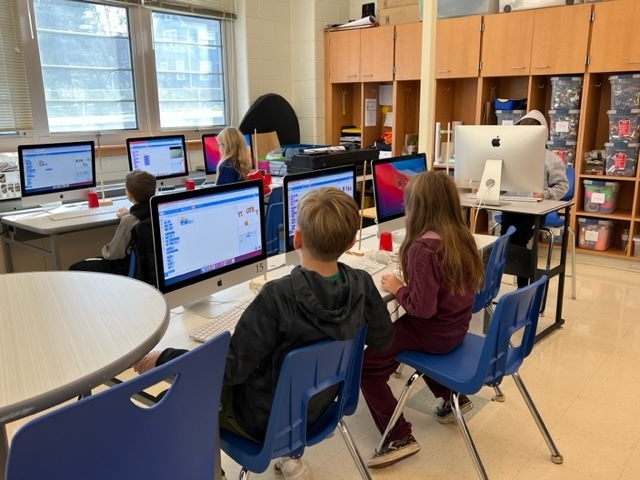 Students working at computer stations writing code using Scratch